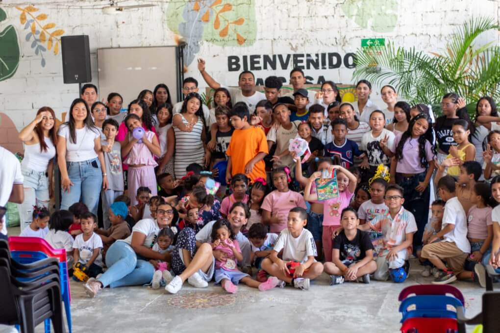 Grupo de niños, niñas y jóvenes universitarios posan en el Comedor Mateo durante la celebración del Día del Niño.